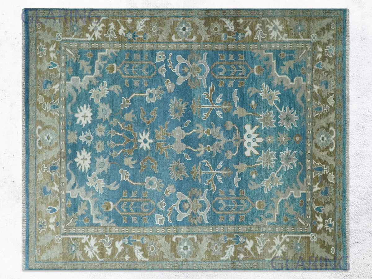 Blue hand knotted oushak rug with open ivory and sage florals and an olive-taupe border.