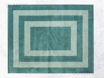 A rectangular modern rug with a border design in teal green, displayed on a neutral background.