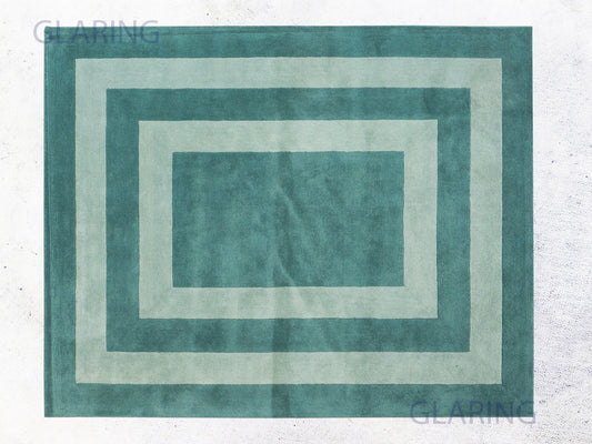 A rectangular modern rug with a border design in teal green, displayed on a neutral background.