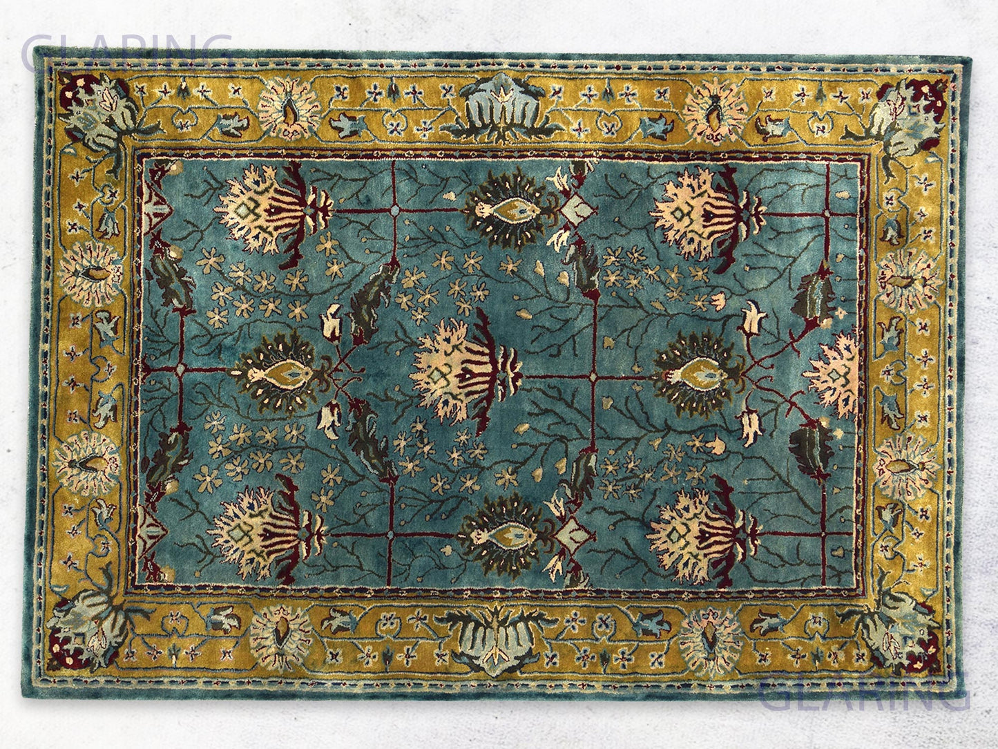 A rectangular traditional teal blue rug with a Persian design, featuring gold, green, and red colors, and floral patterns.