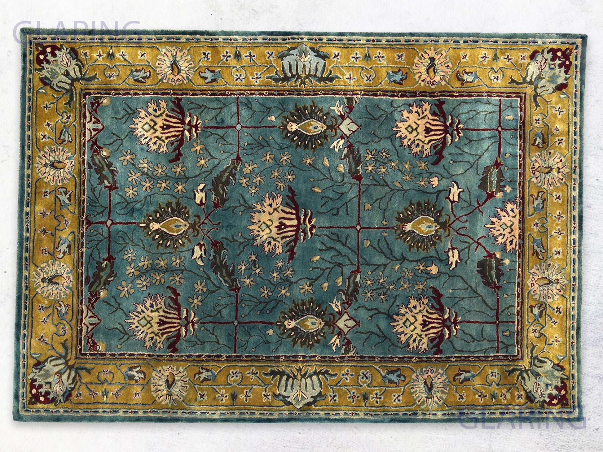 A rectangular traditional teal blue rug with a Persian design, featuring gold, green, and red colors, and floral patterns.