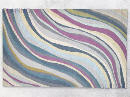 A rectangular rug with an abstract geometric design in shades of grey, purple, blue, and yellow.